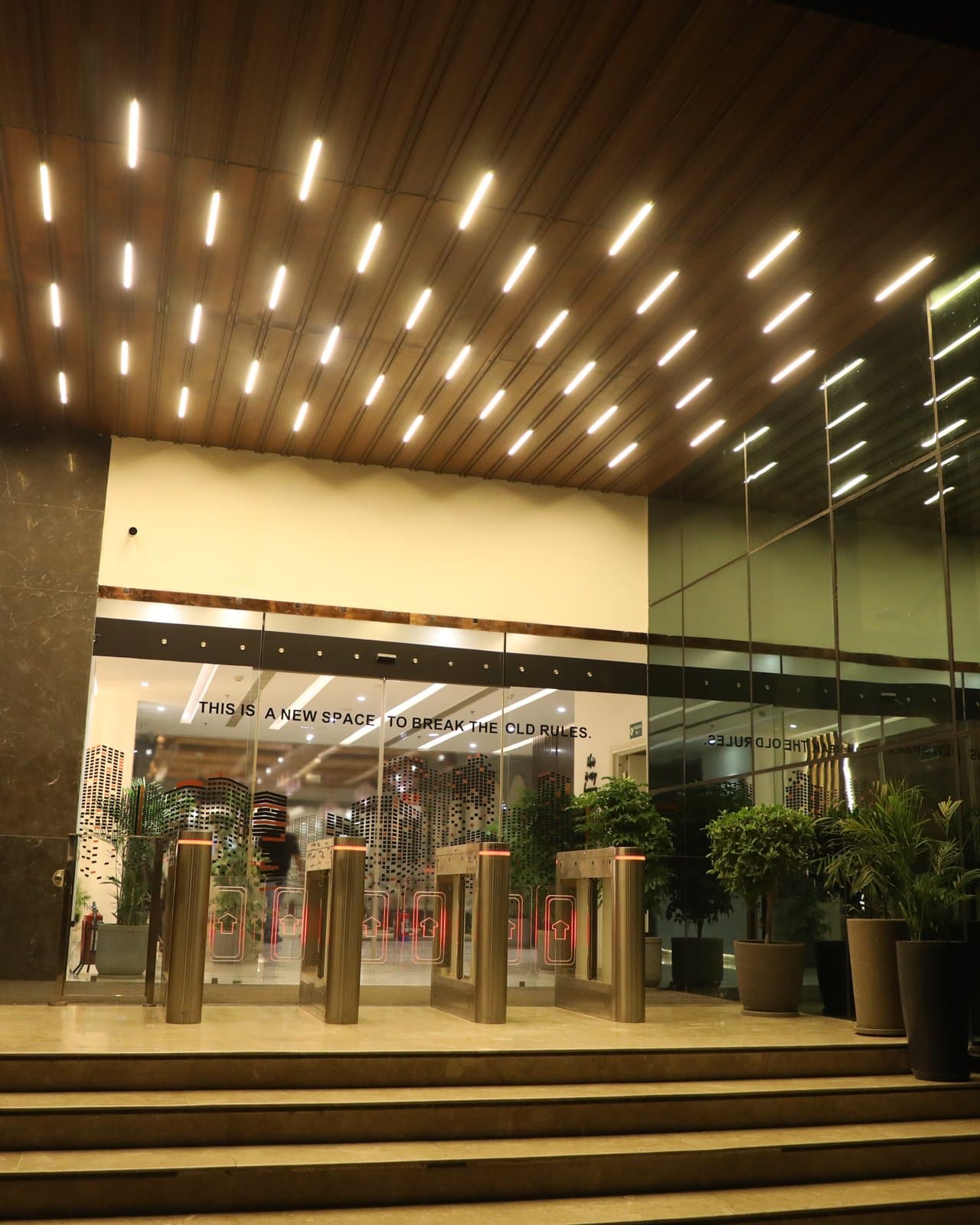 The lit entrance canopy and lobby doors of JDKD Corporate Park at A-23, at night.