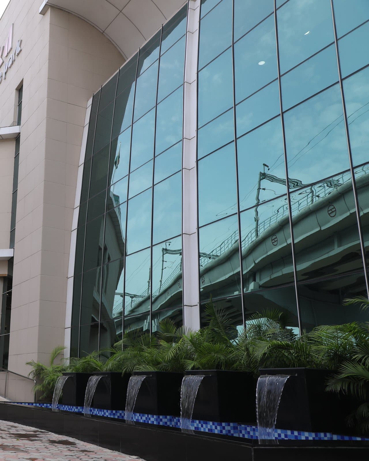 The green glass elevation of JDKD Corporate Park by day, above a planted water feature.