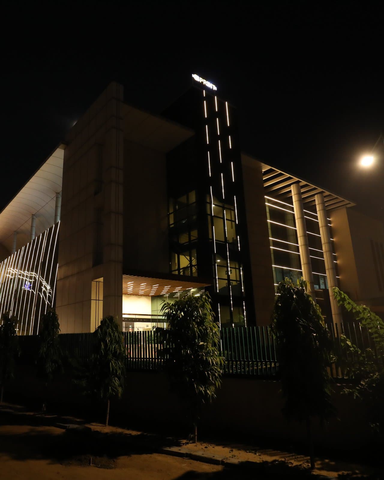 JDKD Corporate Park at A-23 at night, its light-lined tower and entrance canopy.