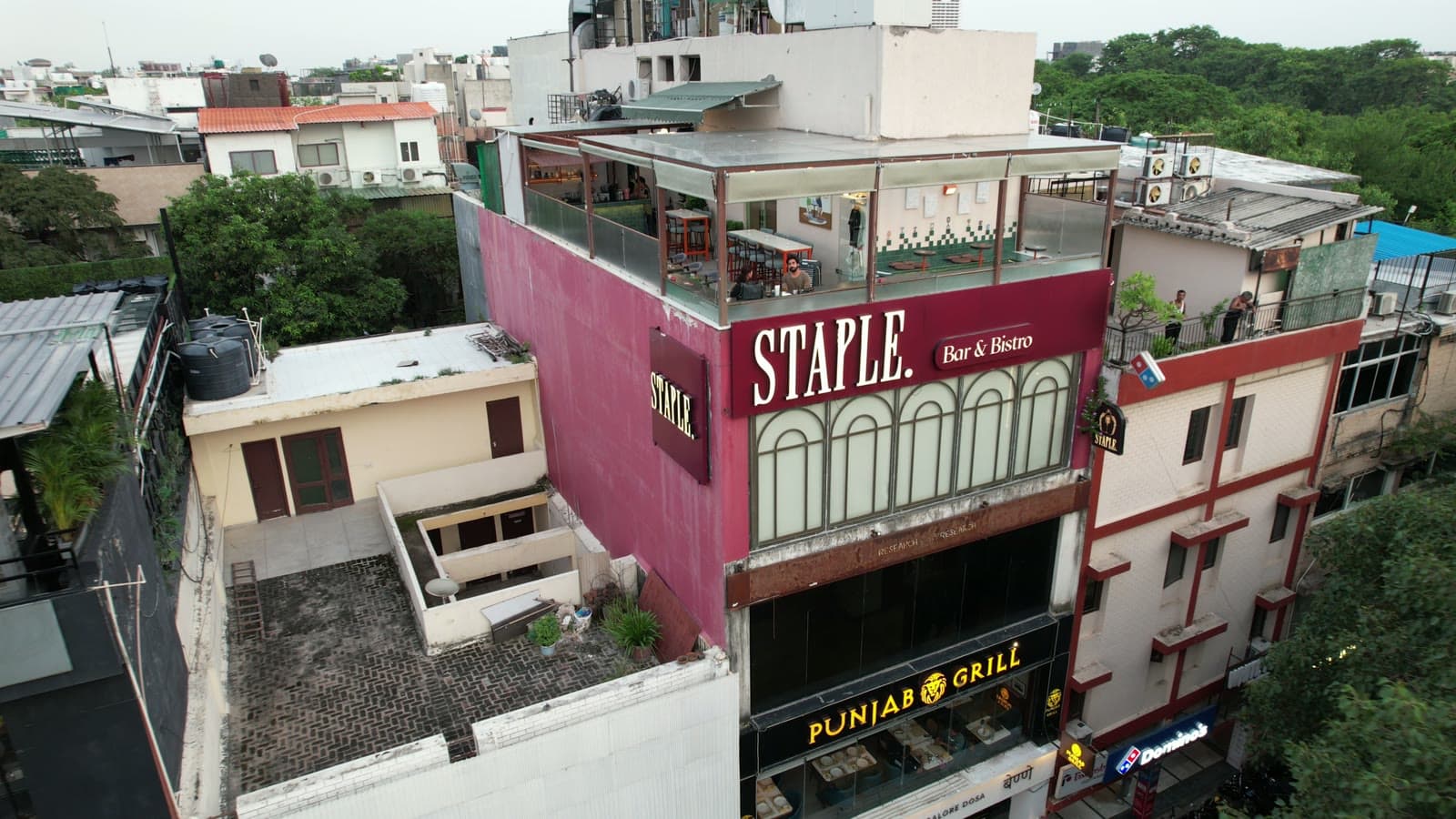 The full M-82 building from the air: Staple Bar & Bistro on the upper floors and rooftop, Punjab Grill and Benne at street level.